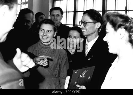 Slaviansk, 1950s, AIZ factory (Armature and Insulator Plant). Female factory worker Kravelis Valentina Timofeevna, wearing a protective work jacket, warmly smiles and interacts with a visiting Japanese delegate wearing glasses. Surrounded by other attentive Soviet workers and management, this lively cultural exchange highlights the friendly international relations, the pride of the dedicated industrial working class, and the engaging diplomatic manufacturing events during the historic post-war era in peaceful Donbas. Stock Photo