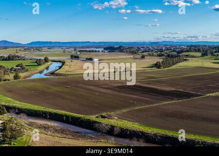 Aerial drone view of rural farmland in Maitland, New South Wales, Australia beneath cloudy blue sky with rainbow visible over agricultural landscape. Stock Photo