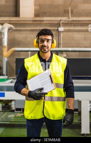 Smiling worker wearing safety vest and earmuffs at factory Stock Photo