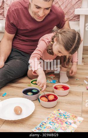Dad and daughter drawing holiday Easter eggs, man and girl toddler spend time together for crafting hobby painting Stock Photo