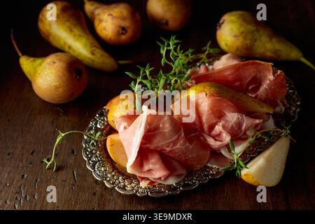 Prosciutto with pears and thyme on a silver tray. Traditional Mediterranean snack with red wine. Stock Photo