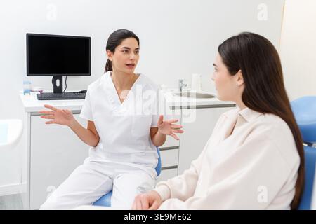 A healthcare professional explains treatment options to a patient in a medical office. The consultation occurs in a modern clinic designed for patient Stock Photo