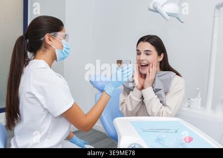 A dental professional demonstrates the results of a treatment to a patient using a mirror. The scene takes place in a dental office, creating an infor Stock Photo