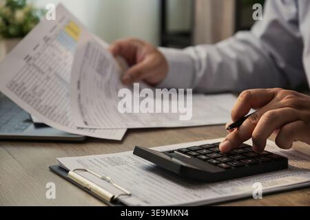 Close up of businessman using calculator and reviewing financial documents on desk, analyzing business report, accounting data, and tax paperwork in m Stock Photo