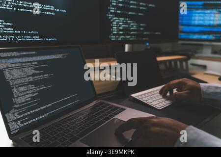 Close up of coding workstation with laptop and multiple screens displaying software code, showing programming workflow, software development, technica Stock Photo