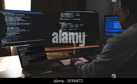 programmer working at a multi monitor computer setup with code on screens in a dark workspace, illustrating software development, coding, debugging, a Stock Photo