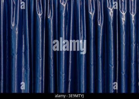 Blue curtain with glossy surface forming vertical folds in interior. Stock Photo