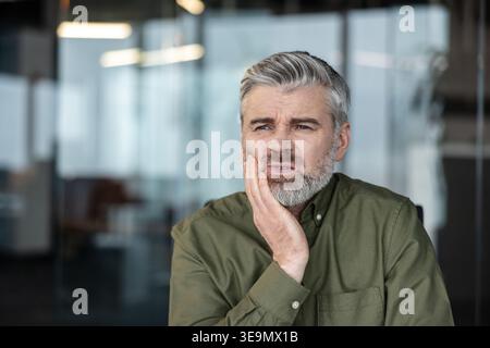 Mature man experiencing intense toothache and dental pain, holding his hand to his cheek in discomfort, highlighting health issues and needing urgent dental care Stock Photo