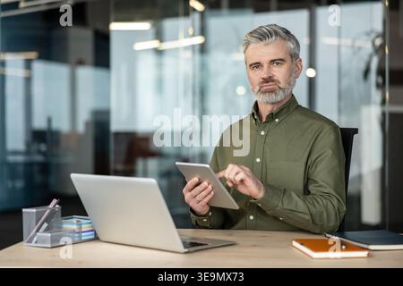 Serious male professional using a digital tablet at his office desk, embracing technology for business operations and efficient communication in a contemporary workspace Stock Photo