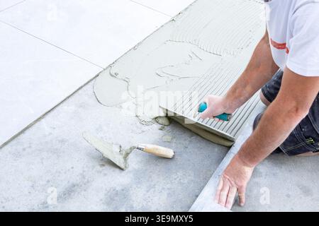 Construction worker applying and combing tile adhesive on a concrete surface before installing large outdoor ceramic tiles. Stock Photo