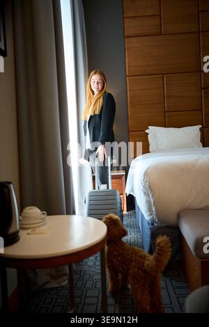 Happy woman with dog in hotel room during daytime Stock Photo