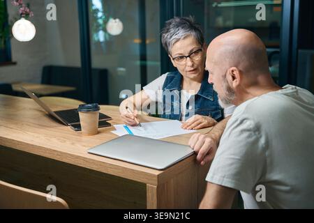 Middle-aged woman discussing documents with man in modern cafe Stock Photo