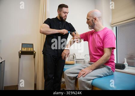 Middle-aged doctor performing reflex test on patient in clinic Stock Photo