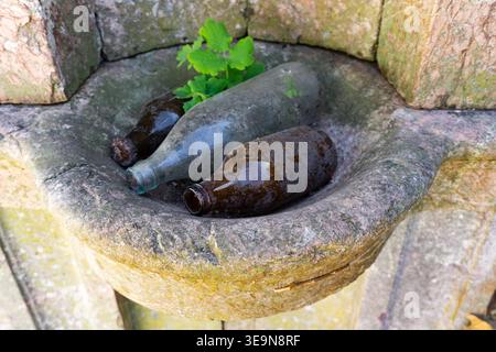 3 old dusty glass bottles resting in a stone bowl at castle Schloss Liebenstein in Brandenburg, Germany Stock Photo