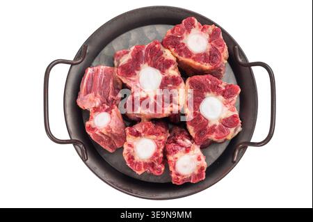 Raw beef oxtail pieces in metal pan with thyme on isolated background, top view butcher style preparation for stew. Stock Photo