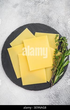 Yellow sliced cheese arranged on black slate platter with herbs on light stone background, rustic dairy food with copy space. Stock Photo
