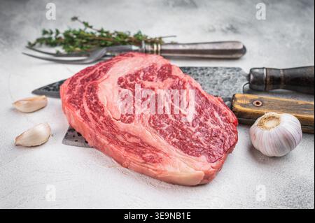 Fresh raw ribeye steak entrecote style with heavy marbling garlic and thyme. Premium beef cut on light stone background Stock Photo