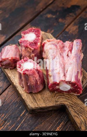 Lamb oxtail sections ready for cooking with herbs on wooden cutting board, overhead composition on dark wood surface. Stock Photo