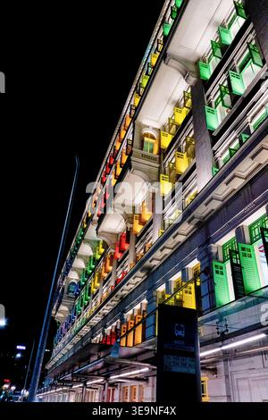 Illuminated building facade at night. Vibrant lights cascade down stone structure. Green, yellow, and red hues glow vividly. Urban architecture under Stock Photo