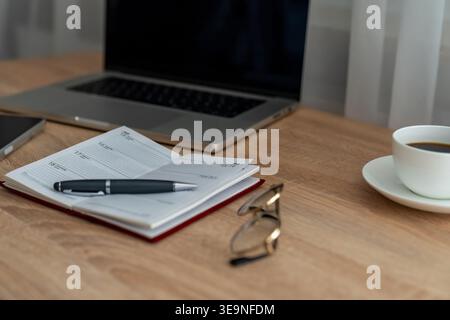 Open planner accompanied by cup of coffee and glasses. Pen resting on open weekly planner with coffee and glasses close by. Journal is open with Stock Photo