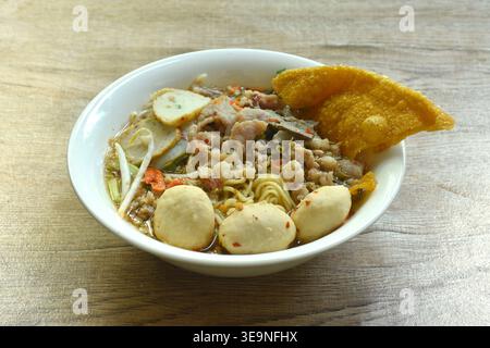 Chinese egg yellow noodles topping chop pork and meatball with crispy fried dumpling paste in spicy tom yum soup on bowl Stock Photo