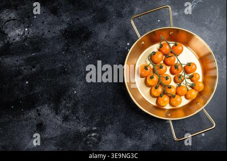 Ripe cherry tomatoes cluster in brass skillet on black rustic surface, top view food background with space for text. Stock Photo