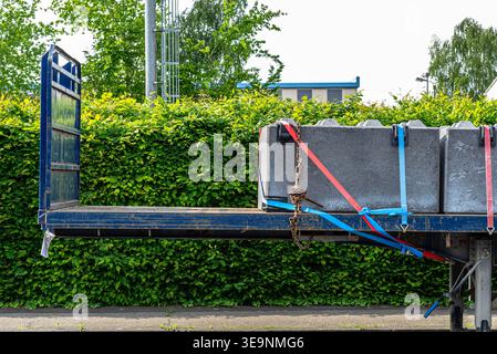 Concrete blocks strapped onto a flatbed trailer for heavy load transport against green hedge Stock Photo