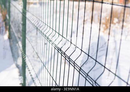 Green metal wire mesh fence standing in focus against a blurred background of snow, defining a boundary Stock Photo