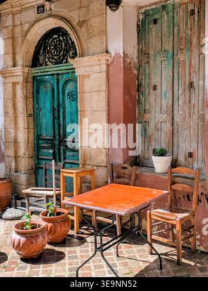 empty table and chairs outside faded wooden door Stock Photo