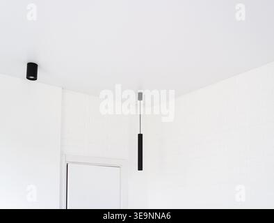 Minimalist interior showcasing modern black linear pendant and spot lights against a white brick wall and clean ceiling Stock Photo