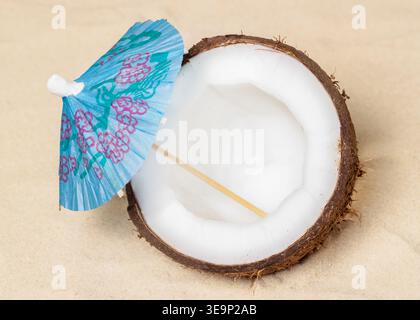 Half coconut with little blue umbrella lying on the sand Stock Photo