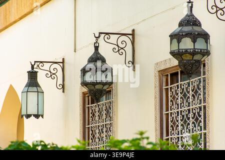 Row of traditional ornate metal hanging lanterns on a textured exterior wall with decorative wrought iron window grilles. Stock Photo