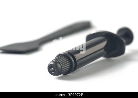 black thermal grease syringe nozzle isolated white background, applicator tip with spreader spatula in soft focus, side view, pc building concept Stock Photo