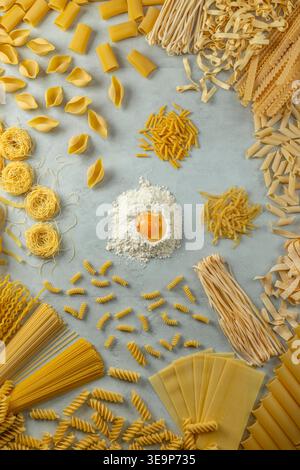 Variety of uncooked pasta, flour, and a raw egg yolk ready for making fresh pasta Stock Photo