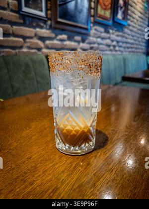 A glass of liquid with a brownish color and a white rim. The glass is on a wooden table Stock Photo