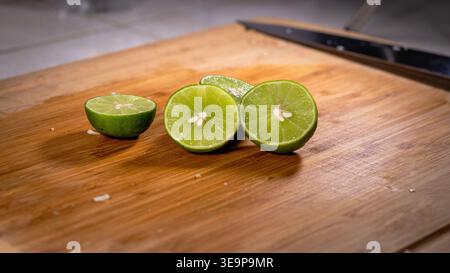 Close-up of fresh green limes cut in half, placed on a wooden cutting board with seeds visible, ready for cooking or juicing. Stock Photo