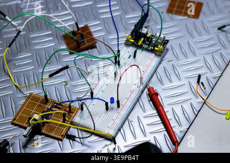 A black multimeter is on a table with wires and other electronic components. The multimeter is displaying the time as 10:05 Stock Photo