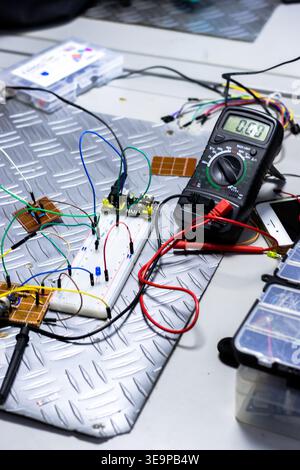 A black multimeter is on a table with wires and other electronic components. The multimeter is displaying the time as 10:05 Stock Photo