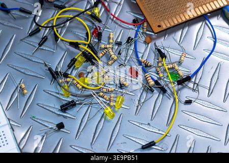 A pile of electronic components on a metal surface. The components include wires, resistors, and capacitors. Concept of disorganization and chaos, as Stock Photo