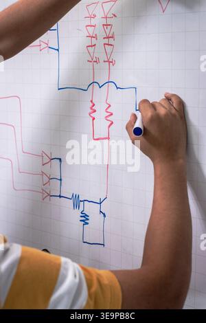 A person is drawing a circuit diagram on a whiteboard. The drawing is colorful and includes a red and blue line. The person is using a marker to draw Stock Photo