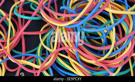 A chaotic tangle of vibrant multicolored elastic rubber bands scattered over a dark surface. Close up. Stock Photo