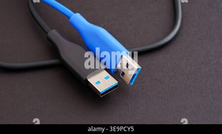 Two USB 3.0 Type-A cables in black and blue colors lying on a dark textured surface. Close up. Stock Photo