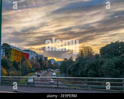 A city street with a bridge over it and a sunset in the background. The sky is cloudy and the sun is setting. Bournemouth, United Kingdom, UK Stock Photo
