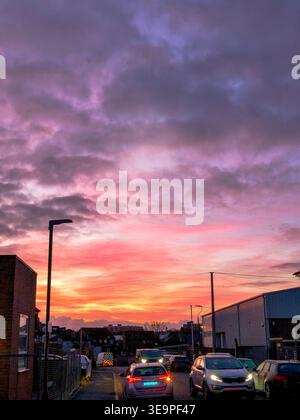 A beautiful sunset with a few cars on the street. The sky is filled with clouds and the sun is setting Stock Photo