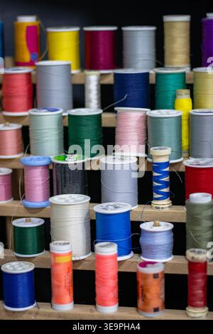A vibrant display of colorful spools of thread arranged neatly on a wooden rack, showcasing an array of hues such as red, yellow, blue, and green. Stock Photo