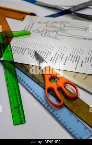 A workspace featuring essential tailoring tools, including vibrant orange scissors, rulers, and a pattern sheet with garment measurements. Ideal for t Stock Photo