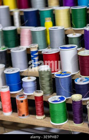 A vibrant display of colorful sewing thread spools neatly arranged on a wooden rack. Perfect for tailoring, crafting, and embroidery projects. Stock Photo