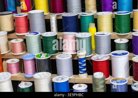 A close-up view of colorful sewing thread spools meticulously arranged on a wooden rack. Perfectly organized for sewing, embroidery, and crafting proj Stock Photo
