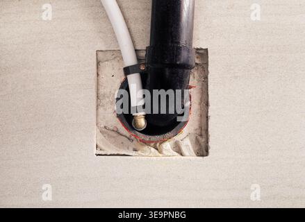 Plumbing drain pipes in tiles floor. Black pvc and white pipe underneath hot water tank in home. Under sink or bathroom drain. Plumbing rough-in Stock Photo