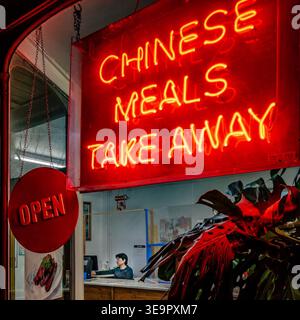 Neon Chinese Takeaway Sign Glowing at Night with Owner alone waiting for customers. Night photo. Urban street Photography.  Bridport, Dorset. Food. Stock Photo